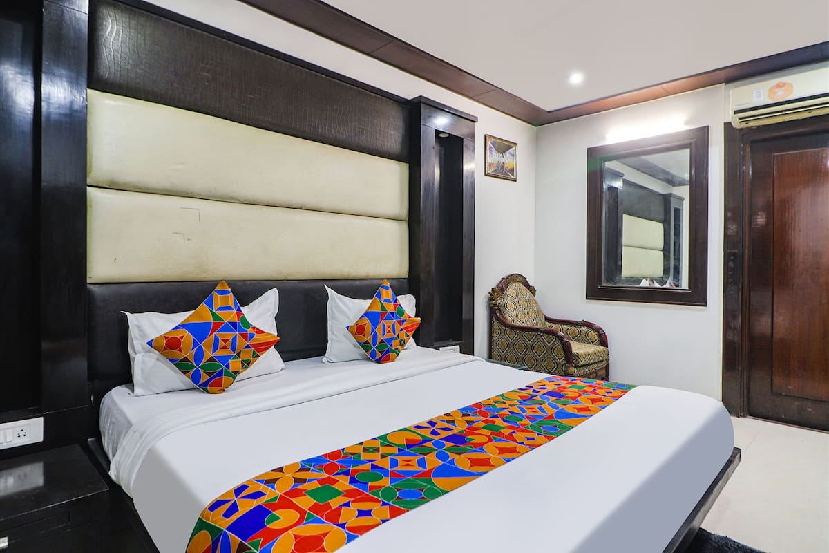 A hotel room with a large bed, a headboard, a chair, and a mirror.