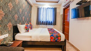 A hotel room with a bed, a TV mounted on the wall, and a window with curtains. - Fabexpress 24 Plus (Bengaluru)
