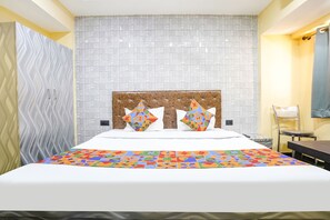 A hotel room with a bed, a headboard, a patterned wall, and a chair. - Fabexpress Kirtiraj (Panvel)