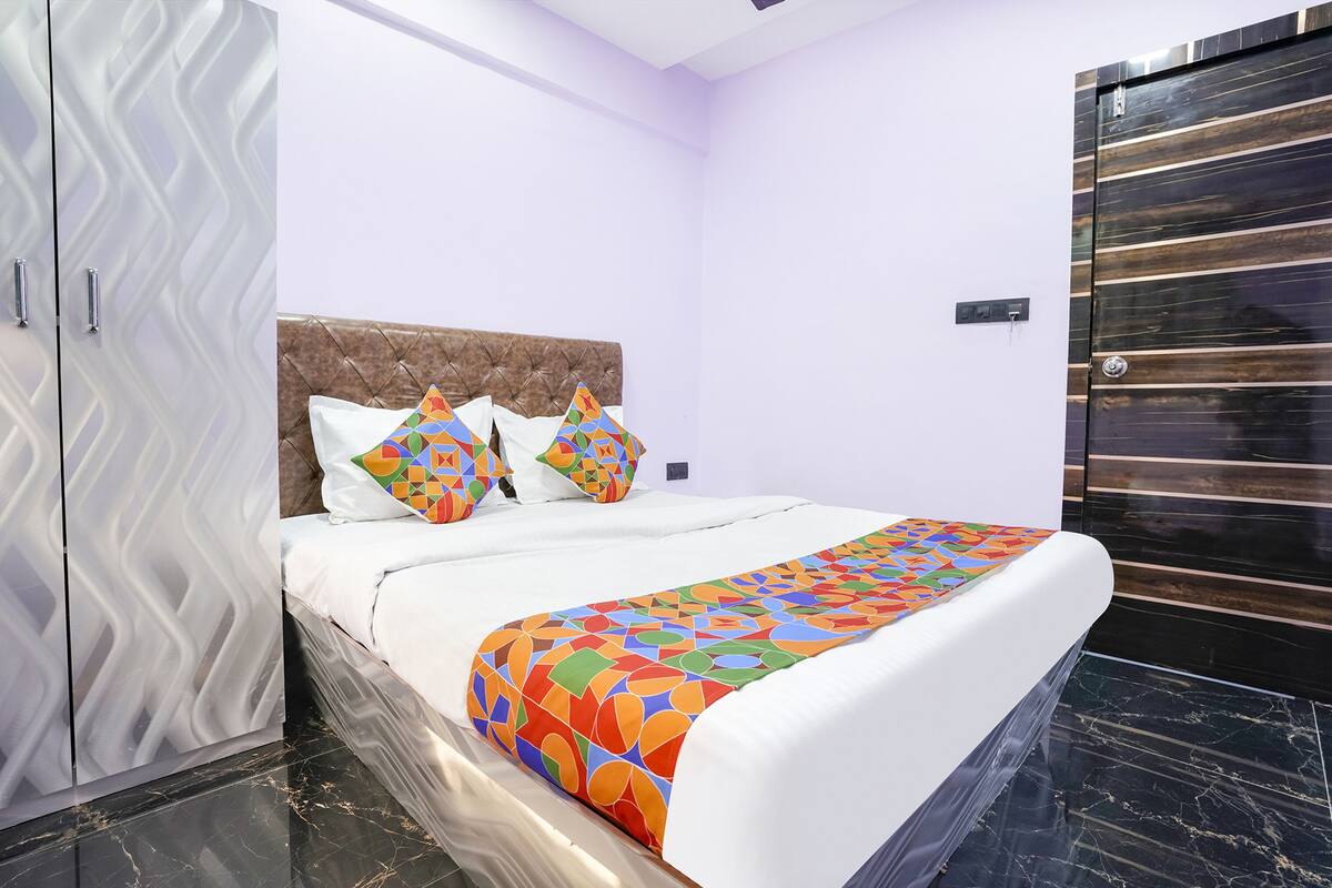 Cama bem arrumada com colcha de padrão geométrico colorido, cabeceira estofada e duas almofadas decorativas.