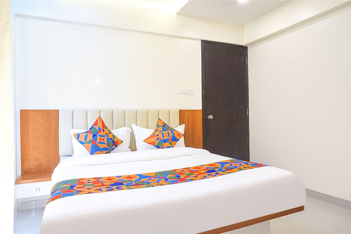 Quarto de hotel com uma cama, cabeceira de madeira, porta escura e parede branca.