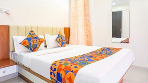 A neatly made bed with a colorful geometric-patterned bedspread, a headboard with a wooden finish, and a single bedside table with a drawer. - Fabhotel Majestic Luxurious (Pune)