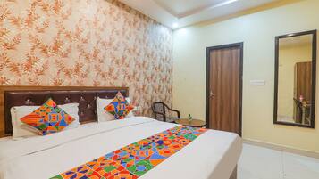 Habitación de hotel con una cama grande, cabecero de madera, papel tapiz floral, un espejo y una pequeña mesa con una silla.