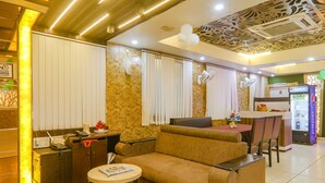A modern living room with a sofa, a small round table, and a dining area with a table and chairs. - Fabexpress Grand Inn (Lucknow)