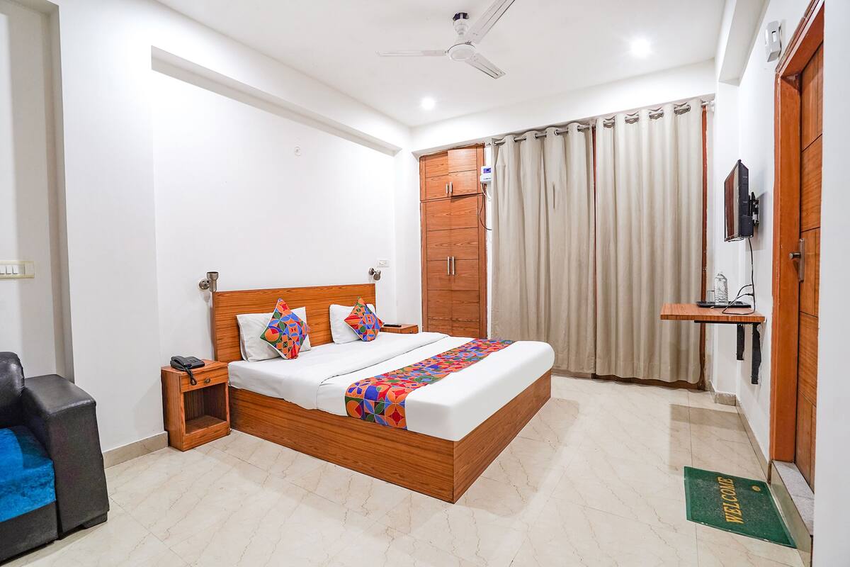 A bedroom with a wooden bed, a nightstand, a desk, a chair, a ceiling fan, and a TV mounted on the wall.