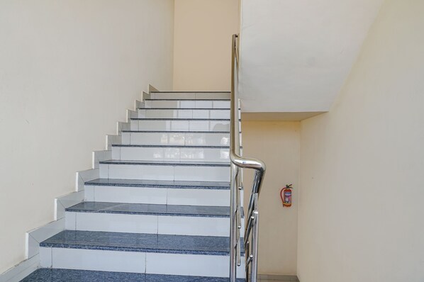 A staircase with a metal handrail and a fire extinguisher mounted on the wall. - Fabexpress Vaishnav Inn (Mawal)