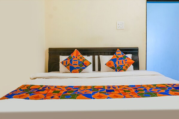 A bed with a colorful geometric-patterned bedspread and two decorative pillows. - Fabexpress Vaishnav Inn (Mawal)