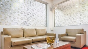 A modern living room with two beige leather sofas, a wooden coffee table with a newspaper, and a decorative golden bowl. - Fabhotel Grey Inn (Pune)