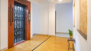 A hallway with a wooden door, a potted plant, and a wall with a decorative panel. - Fabhotel Grey Inn (Pune)