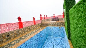 A pool with blue mosaic tiles, a red fence, and a statue on a platform. - Fabhotel Nirvana Grand By Io (Amritsar)