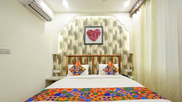 A hotel room with a bed, a headboard with a heart-shaped decoration, and a patterned bedspread.