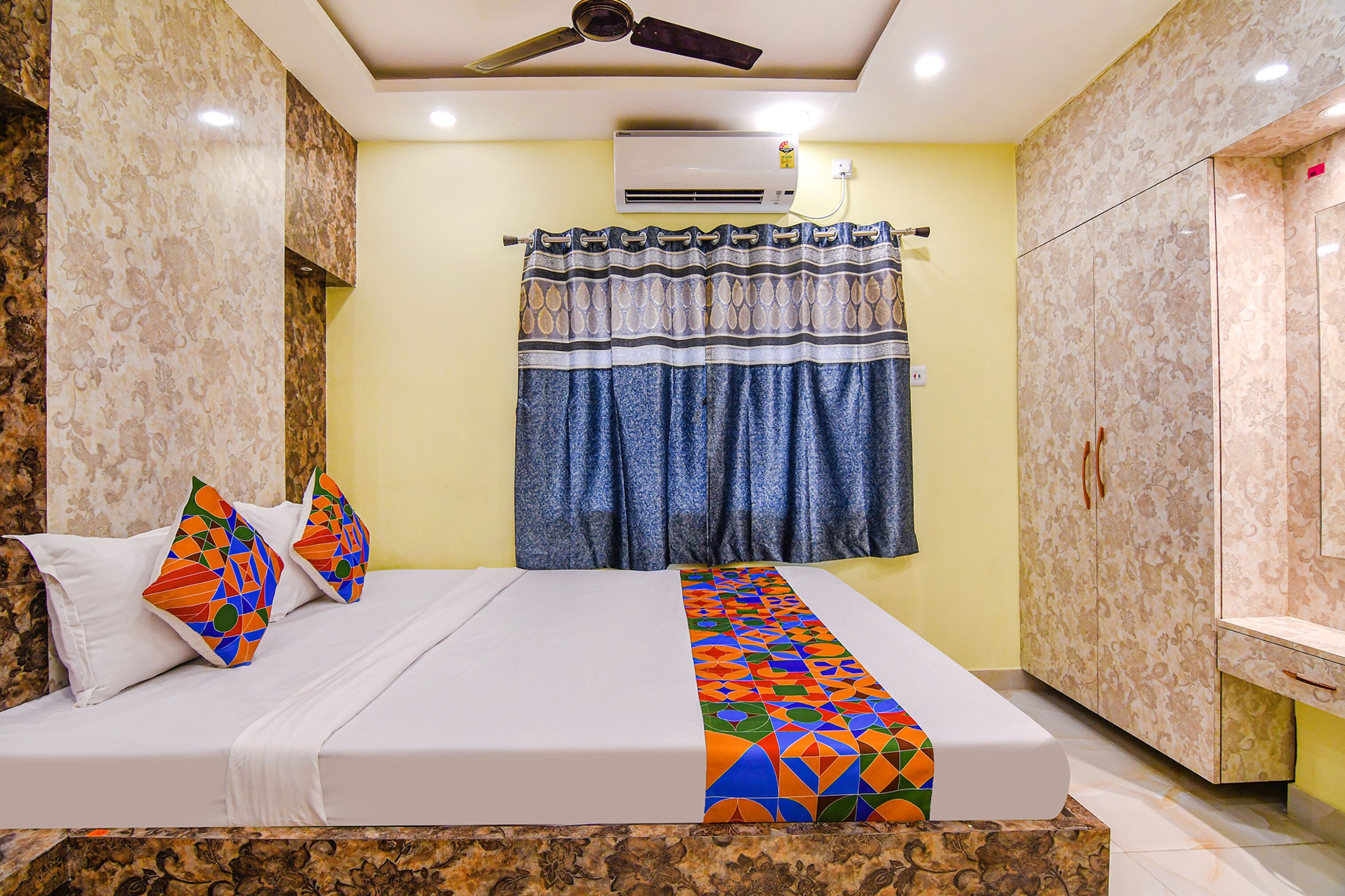 A hotel room with a bed, a ceiling fan, an air conditioning unit, a curtain, and a wardrobe.