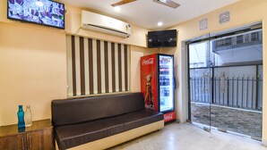 A reception area with a sofa, a Coca-Cola refrigerator, a television, and a ceiling fan. - Fabhotel Divine Chariot (Barasat)