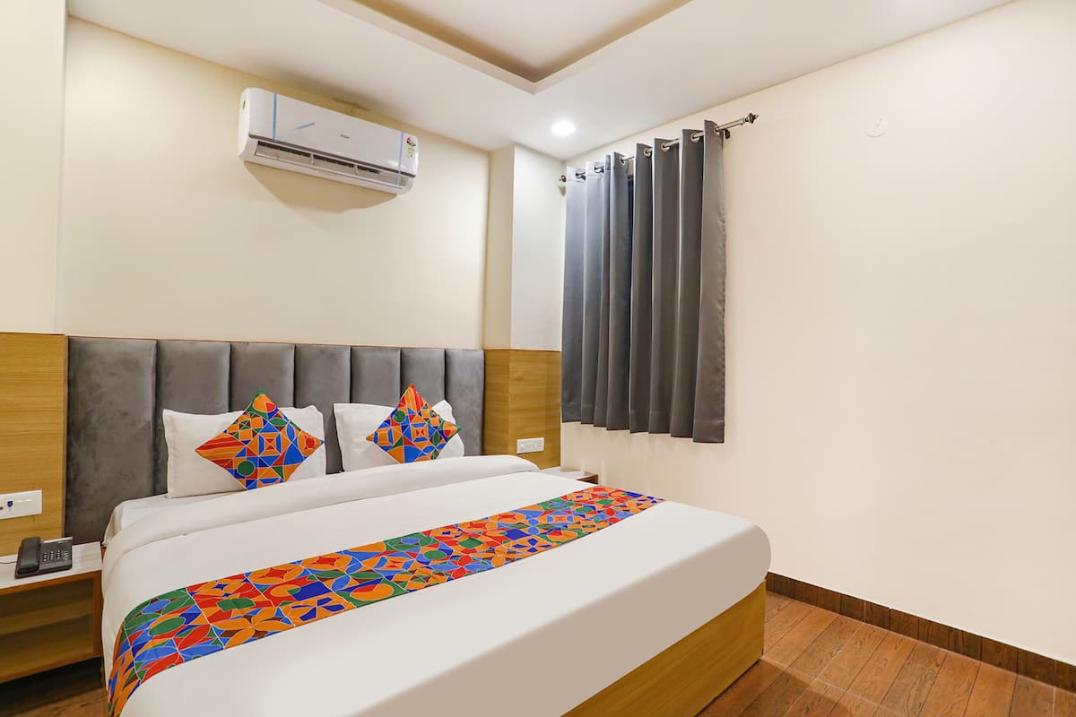 Habitación de hotel con cama, mesita de noche, equipo de aire acondicionado y ventana con cortinas.