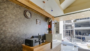 A reception area with a wooden desk, a clock, and a framed picture on the wall. - Fabhotel Js Pearl (Dehradun)