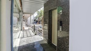 A corridor with a glass door leading to a room, a metal railing, and a textured wall. - Fabhotel Js Pearl (Dehradun)