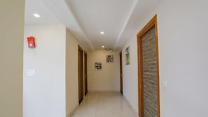A hallway with a tiled floor, wooden doors, and a fire alarm on the left wall. - Fabhotel Js Pearl (Dehradun)
