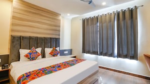 A hotel room with a large bed, a ceiling fan, a nightstand, and a window with curtains. - Fabhotel Js Pearl (Dehradun)