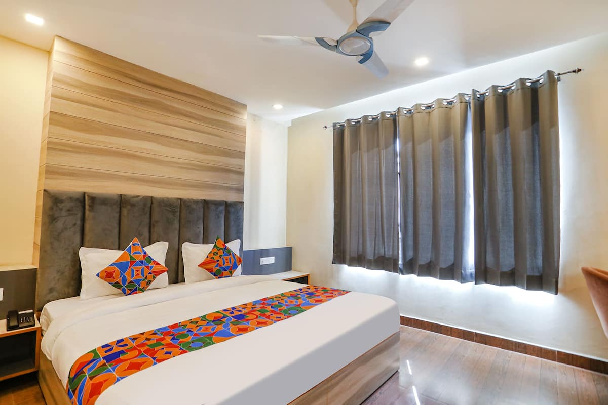 Habitación de hotel con una cama grande, un ventilador de techo, una mesita de noche y una ventana con cortinas.