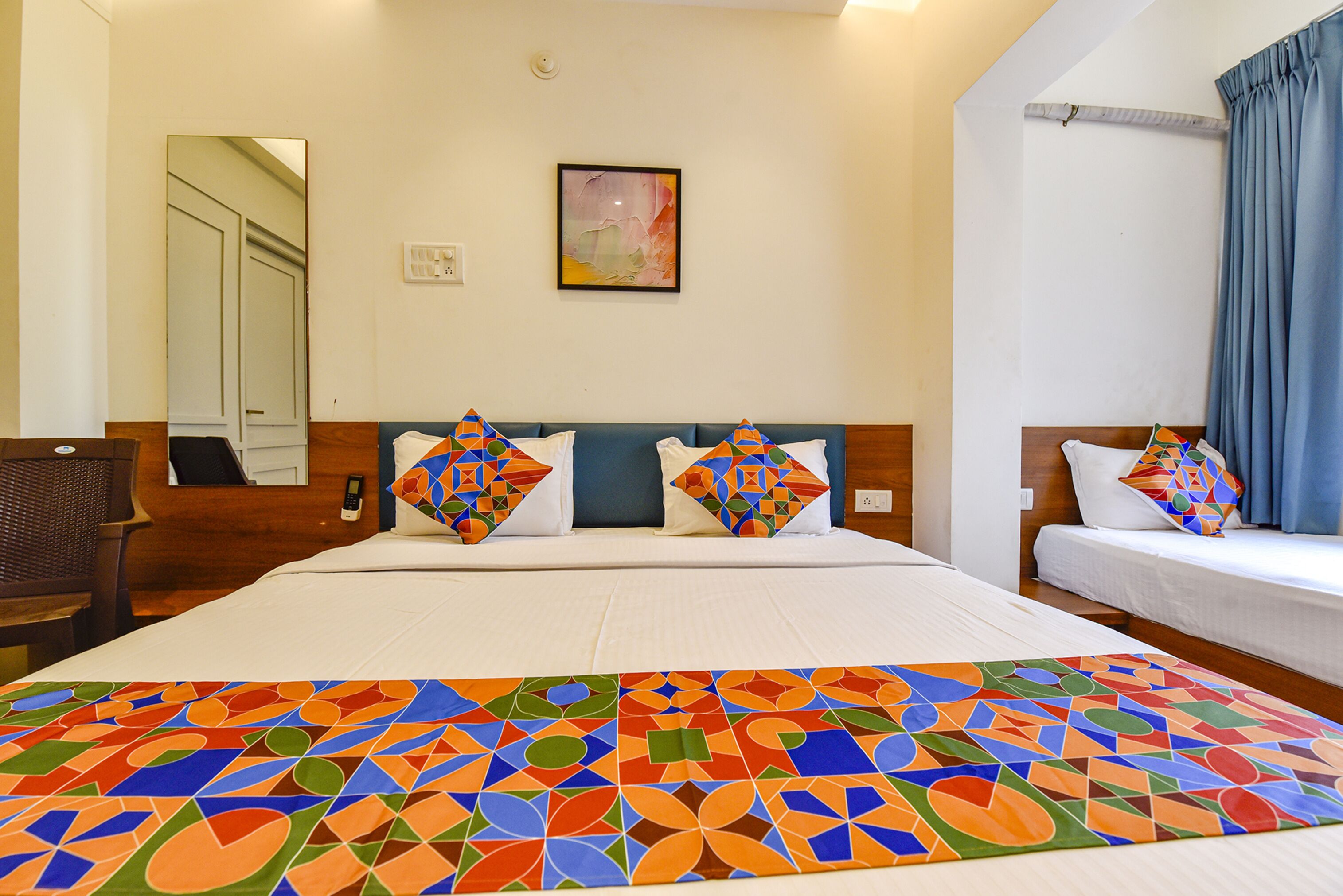 A hotel room with a large bed, two smaller beds, a chair, a mirror, and a painting on the wall.