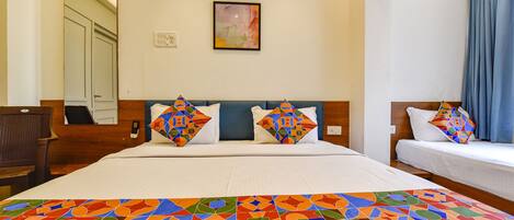 A hotel room with a large bed, two smaller beds, a chair, a mirror, and a painting on the wall.