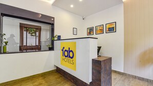 A reception area with a wooden reception desk, a large window with blinds, and three framed artworks on the wall.
