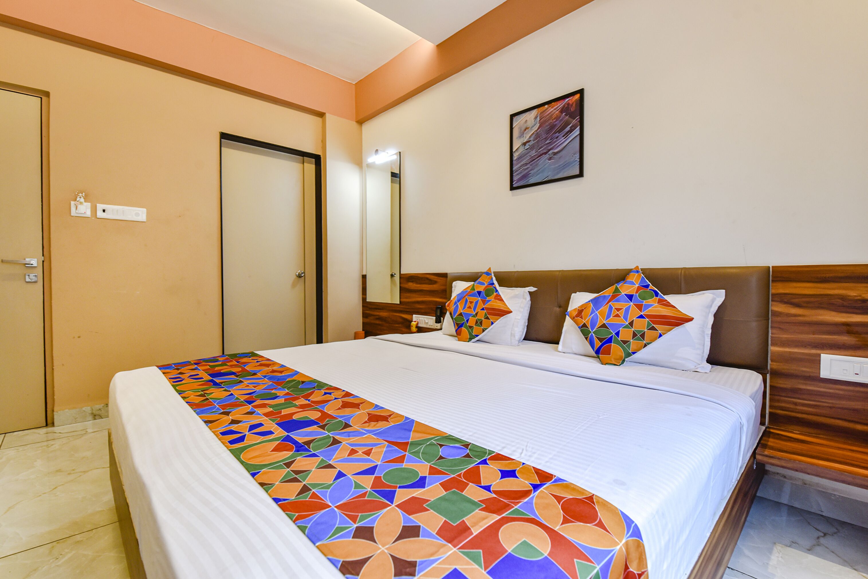Une chambre d’hôtel avec un grand lit, une tête de lit en bois et une couvre-lit aux motifs géométriques colorés.