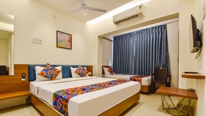 A hotel room with a large bed, a desk, a chair, a television, and a window with curtains.