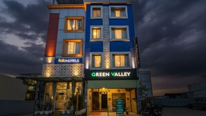 Un hotel de varios pisos con letreros 'fabHOTELS' y 'GREEN VALLEY', que presenta un diseño moderno con una entrada destacada y un área exterior cubierta.
