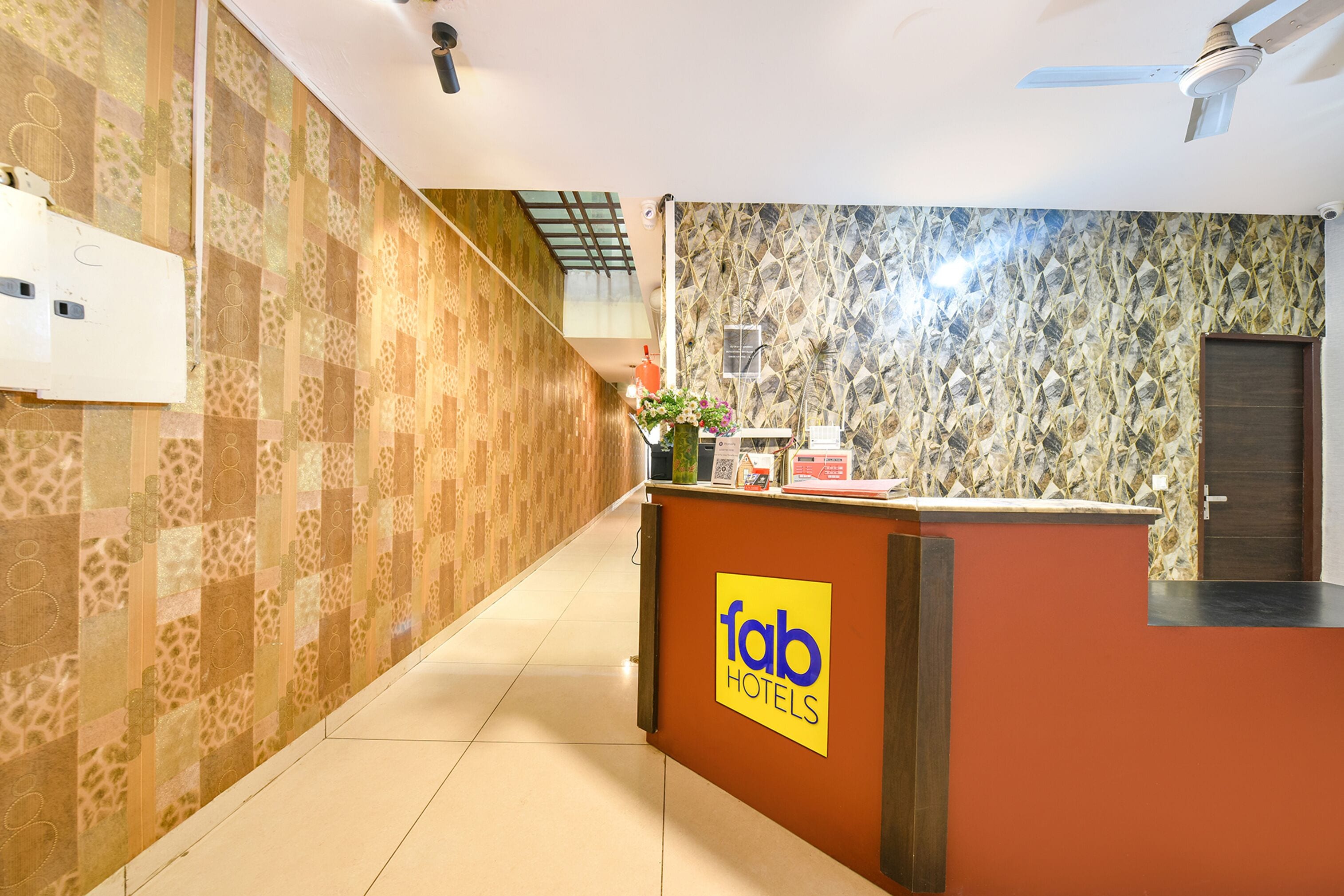 Een hotel receptie met behang, een receptiebalie met de tekst 'Tab Hotels' en een plafondventilator.