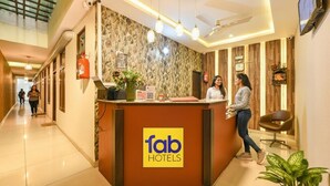 Una recepción de hotel con un cartel de 'fab hotels', un extintor y una planta en maceta.