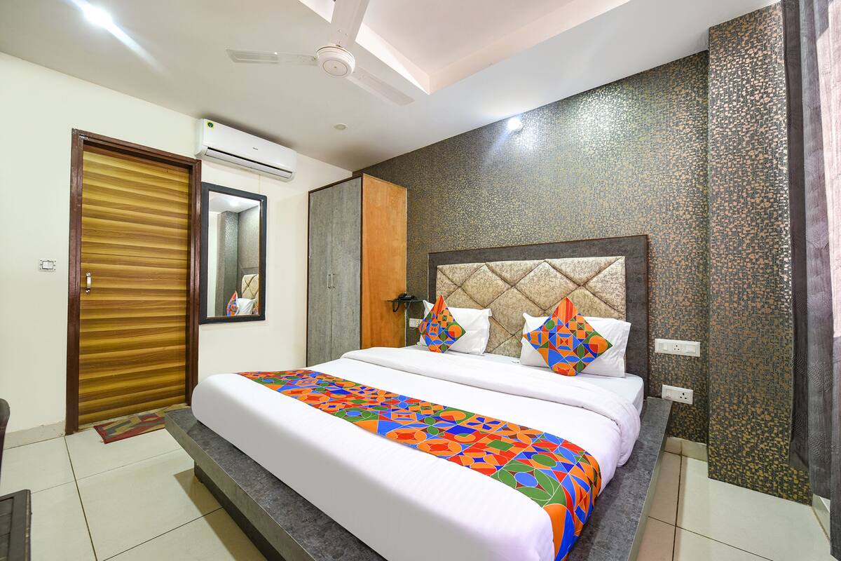 A hotel room with a bed, a wardrobe, an air conditioning unit, and a textured wall.