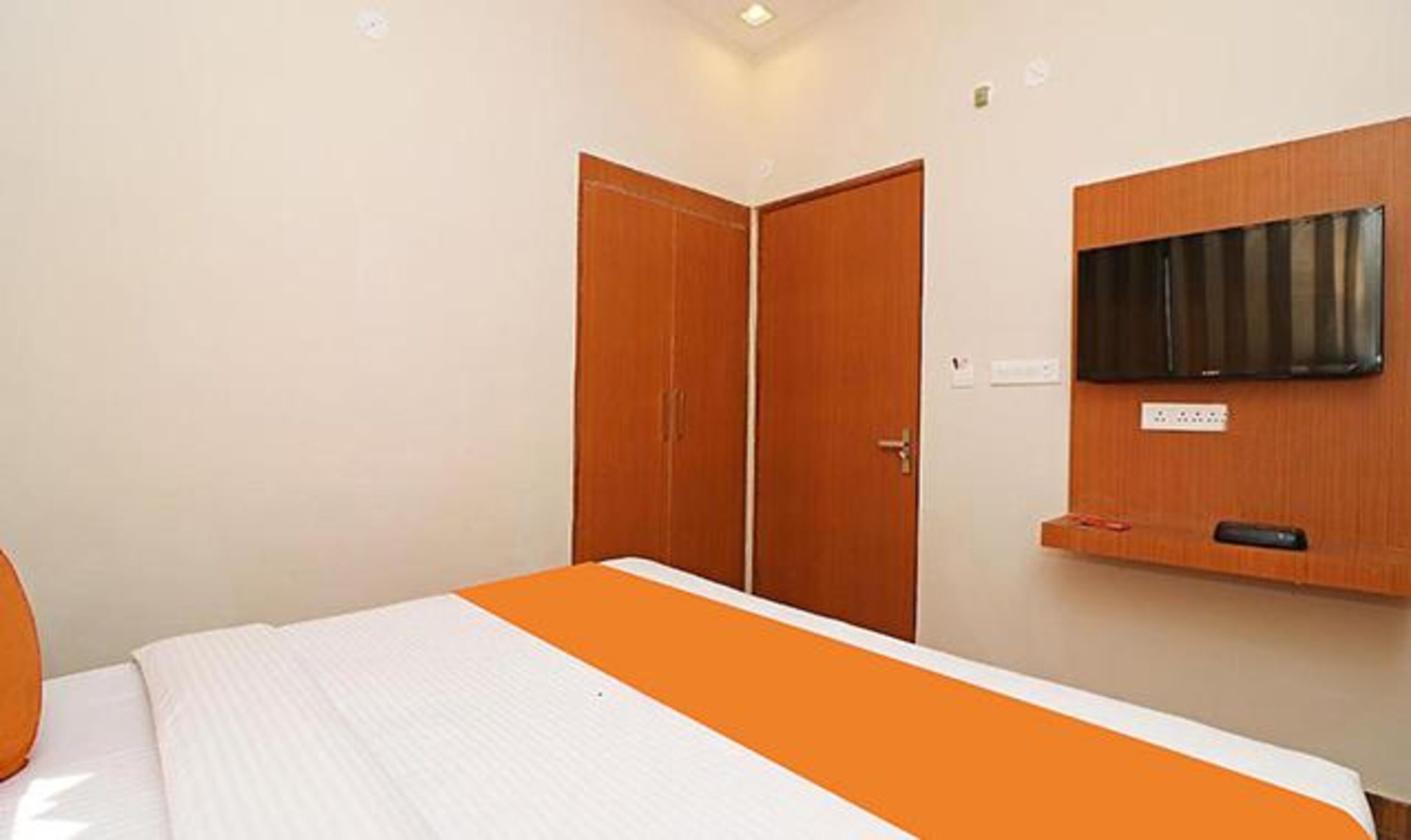A hotel room with a bed, a television mounted on the wall, and a wooden wardrobe.