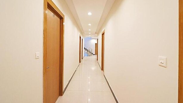 A long, narrow hallway with wooden doors on either side and a tiled floor. - Fabexpress Green Comfort (Dehradun)