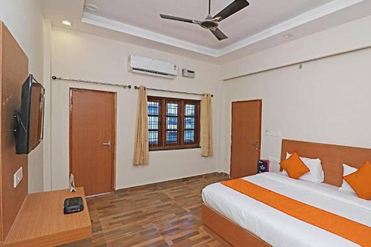 Quarto de hotel com cama, televisão, ar condicionado e janela com cortinas.