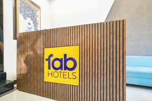 A reception desk with a 'fab hotels' sign, a wooden panel design, and a blue couch in the background. - Fabhotel Prime The Euro (Indore)