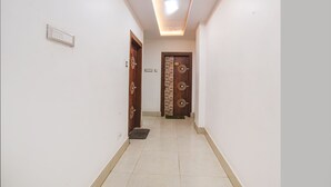 A hallway with two wooden doors, a light switch, and a green mat on the floor. - Fabhotel Raj Niwas (Patna)