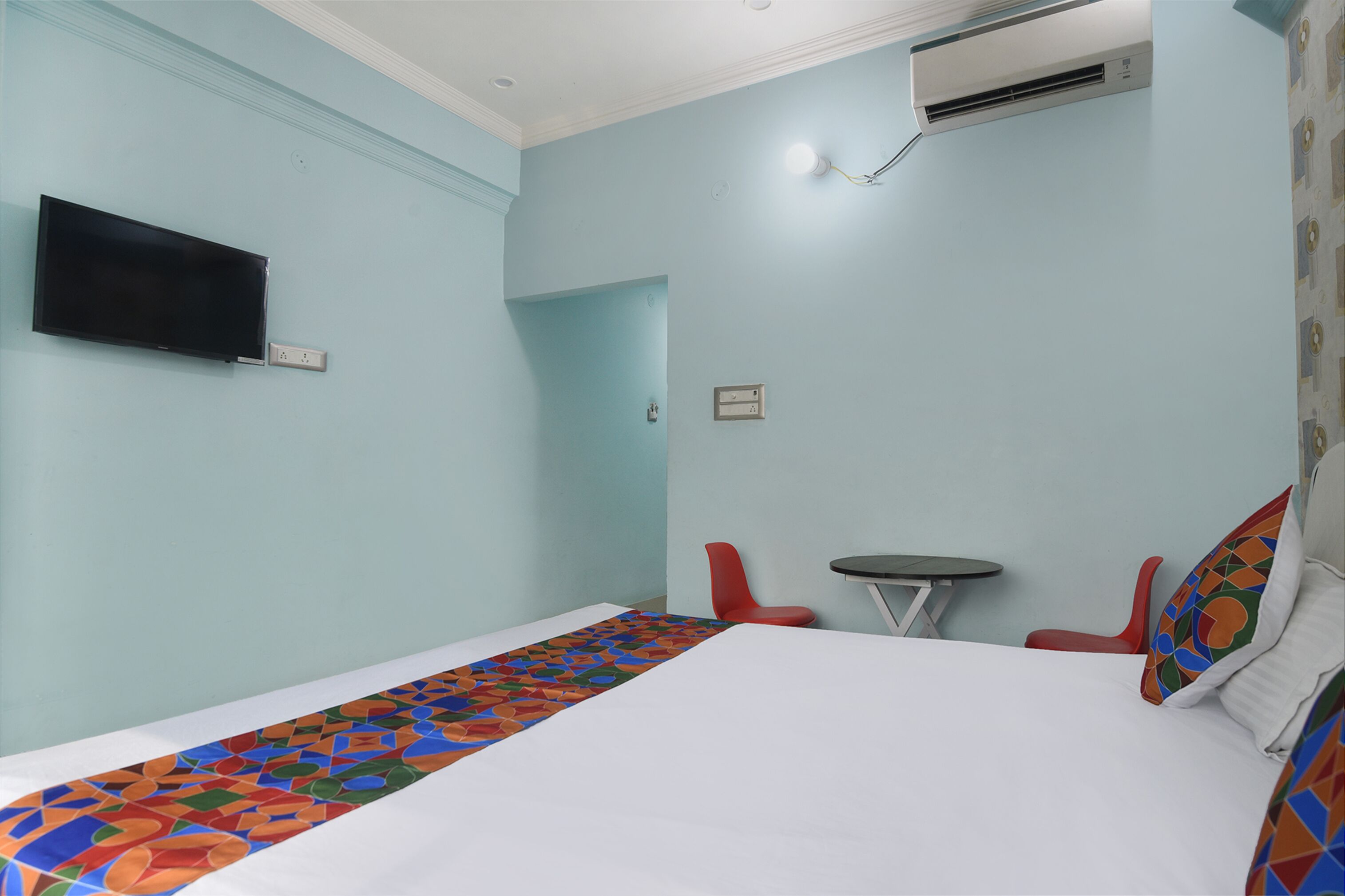 A hotel room with a bed, a TV mounted on the wall, a small table, and a red chair.
