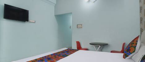 A hotel room with a bed, a TV mounted on the wall, a small table, and a red chair.