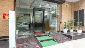 A hotel entrance with a glass door, a red carpet, and potted plants.