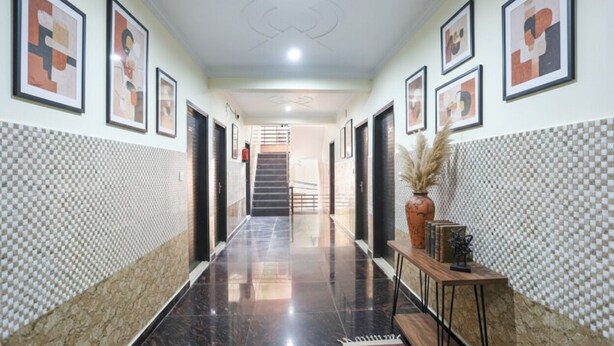 A hallway with a checkered wall pattern, framed artwork on the walls, a polished floor, and a staircase in the background.
