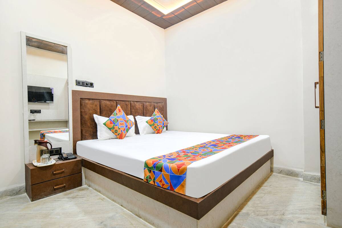 Quarto bem arrumado com cama grande, mesa de cabeceira com abajur e prateleira embutida para TV.
