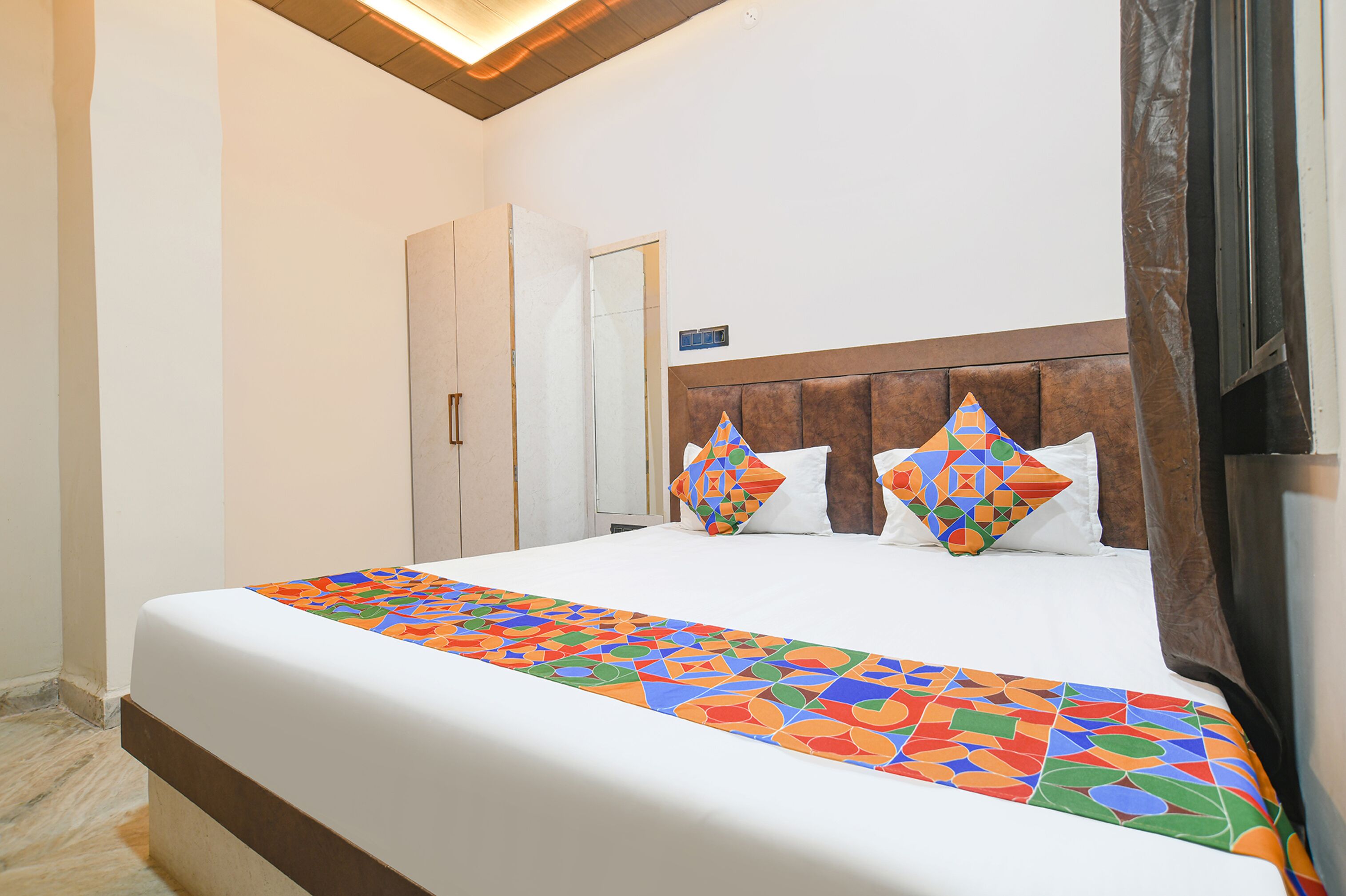 A hotel room with a large bed, a wooden headboard, a mirror, and a wardrobe.