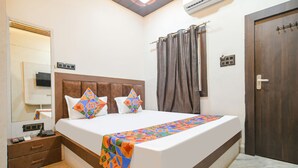 A hotel room with a large bed, a bedside table with a phone and charger, a mirror, and a door with a handle.