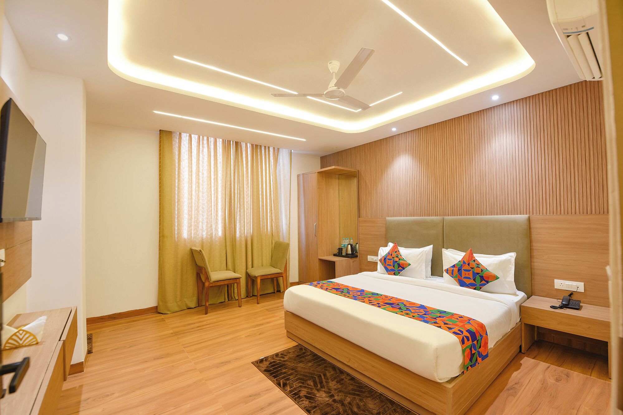 A modern hotel room with a large bed, a ceiling fan, and a wooden wardrobe.