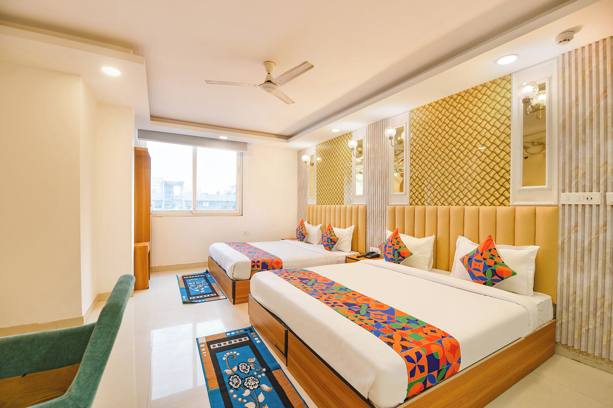 A hotel room with two beds, a desk, and a chair. There is a window with a view of buildings outside.