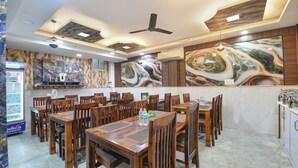 Ein Restaurant mit Holztischen und -stühlen, Marmorbildkunst an den Wänden und Deckenventilatoren.