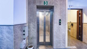 Ein Aufzug mit einem Schild mit der Aufschrift 3, daneben eine Zimmerpflanze und ein digitales Display an der Wand.