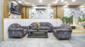 Eine moderne Lobby mit einem Marmor-Empfangstresen, grauen Polstersofas, einem Couchtisch und einem großen Fernsehbildschirm.