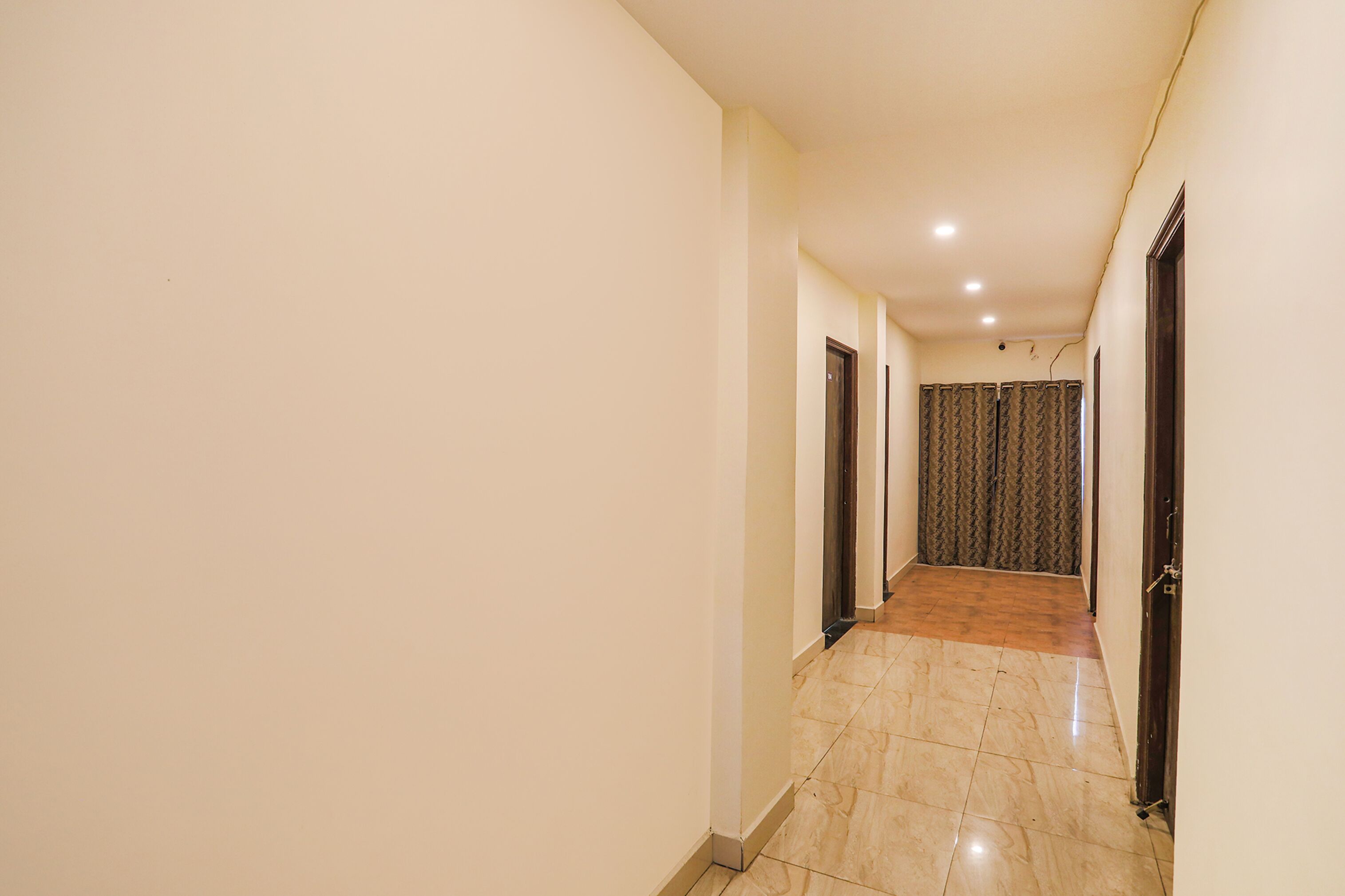 A narrow hallway with a tiled floor, plain walls, and doors leading to rooms.